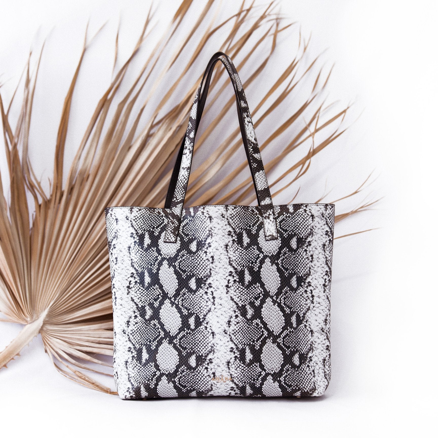 Amana Jeanne Tote front view. Black and grey embossed python print smooth leather tote bag with hidden magnetic fold over closure, leather straps, leather interior, cellphone pocket and zip pocket in front interior, detachable black zip pocket bag.