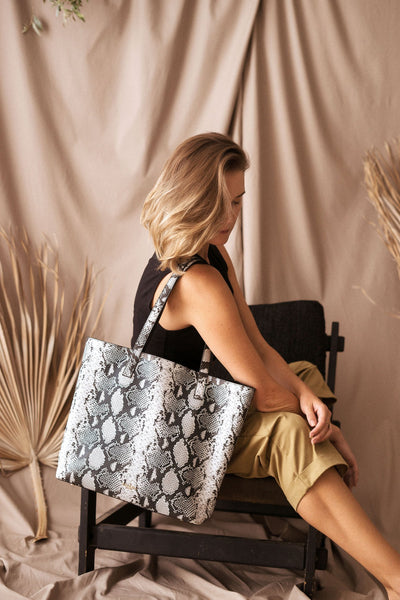 Amana Jeanne Tote Llifestyle image. Jeanne Tote bag draped over women's shoulder who is sitting on a stool.