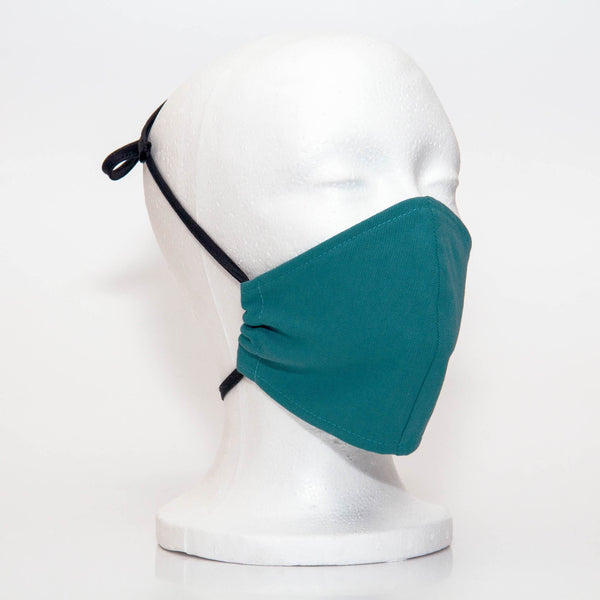 Teal Alpha Mask Side View: Solid teal colour fabric face mask contoured to fit comfortably on your face. This is a 3 layer fabric mask with a middle pocket to insert the filter as the third layer. The bias binding straps is easily adjustable for your comfort and ties behind your head. This mask has a removable filter. This mask an unisex adult fit.