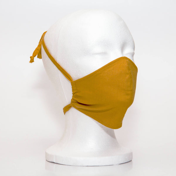 Mustard Alpha Mask Side View: Solid mustard colour fabric face mask contoured to fit comfortably on your face. This is a 3 layer fabric mask with a middle pocket to insert the filter as the third layer. The bias binding straps is easily adjustable for your comfort and ties behind your head. This mask has a removable filter. This mask an unisex adult fit.