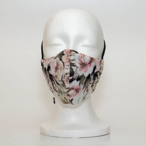 Oltre Print Mask Front View: Pink Peonies print. The striking print of pink peonies gives this mask a soft feminine touch, with muted pink and green tones that will elevate your outfit. 3 Layer fabric mask with a middle filter layer that is contoured to fit comfortably on your face. Mask will fit women and teen girls.