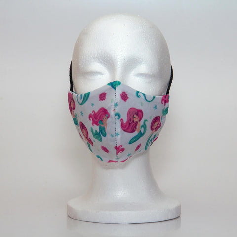 Oltre Print Mask Front View: Mermaids print. The beautiful mermaid print is a pretty interpretation for all the little mermaid fans. 3 Layer fabric mask with a middle filter layer that is contoured to fit comfortably on your face. Mask will fit pre school girls between 3 to 6 years old.